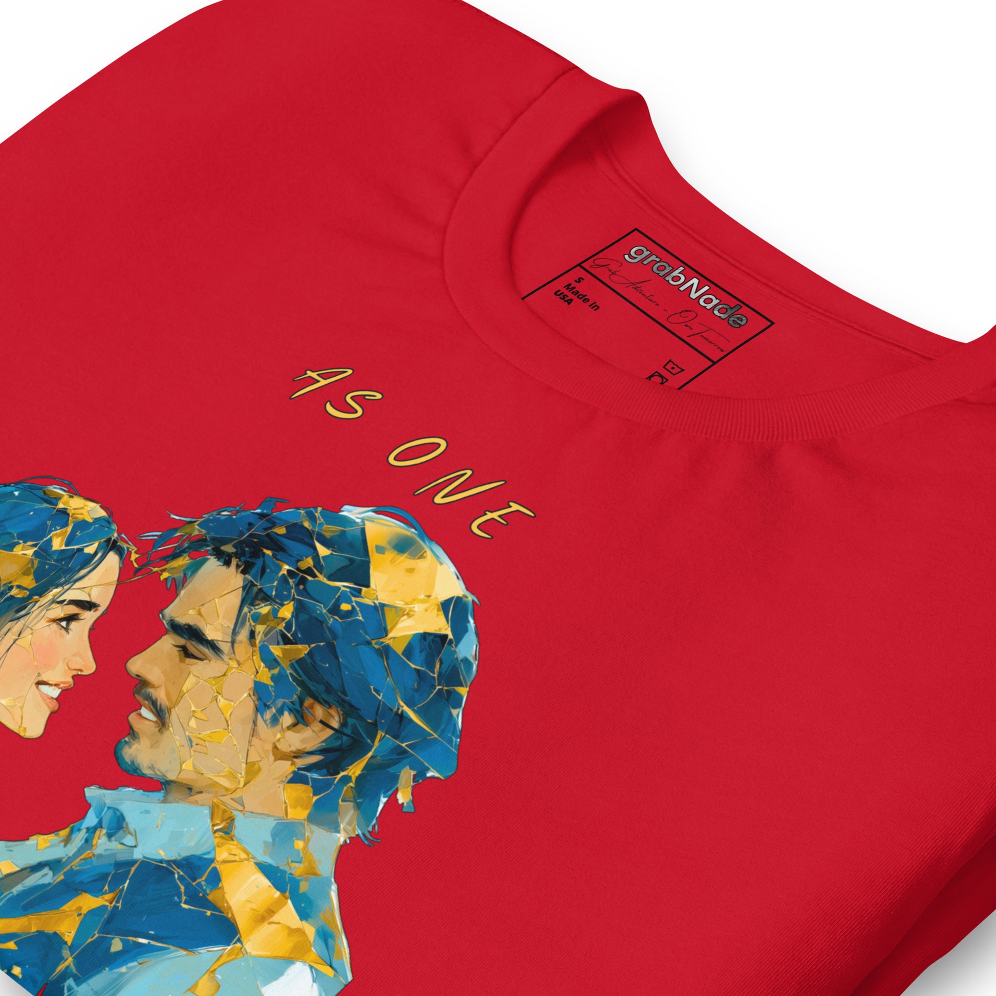Product mockup. Close-up of a red T-shirt showing two stylized faces of a man and woman made from blue and gold geometric shards, with the text “AS ONE” above.