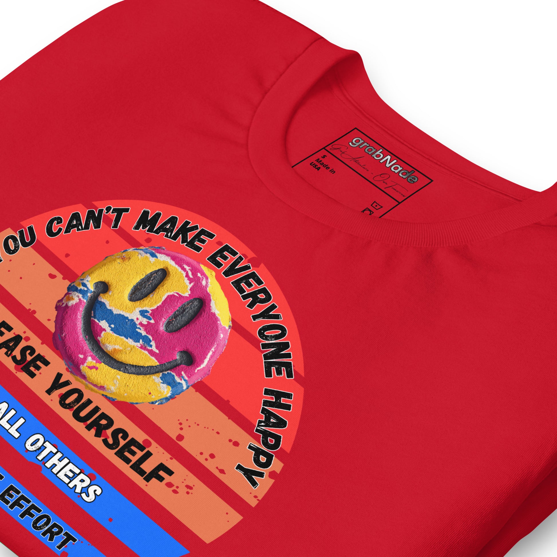 Product mockup. Close-up view of a red T-shirt with a large multicolored smiley face graphic and the text "YOU CAN'T MAKE EVERYONE HAPPY, PLEASE YOURSELF, AND ALL OTHERS WORTH THE EFFORT".
