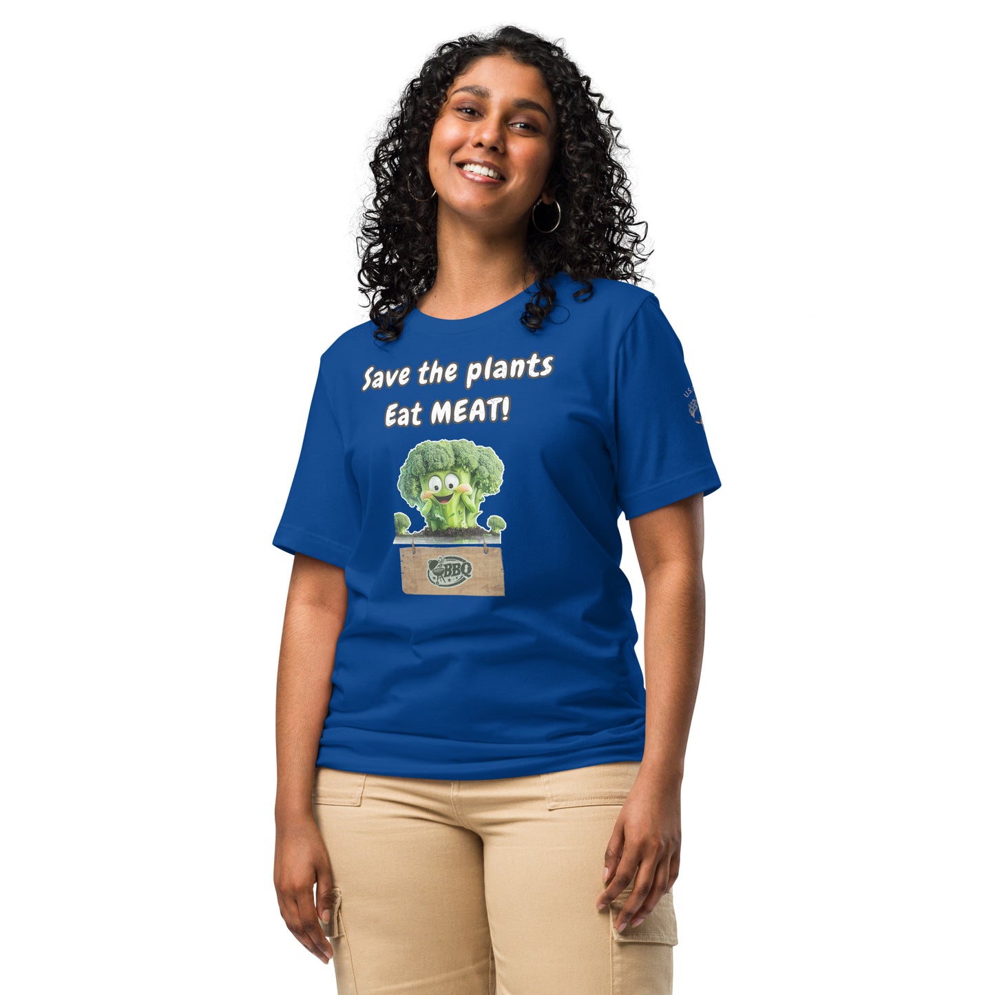 Product mockup. A woman wearing beige pants and a royal blue T-shirt with a happy cartoon broccoli and the phrase “Save the plants Eat MEAT!” on the front, standing upright.