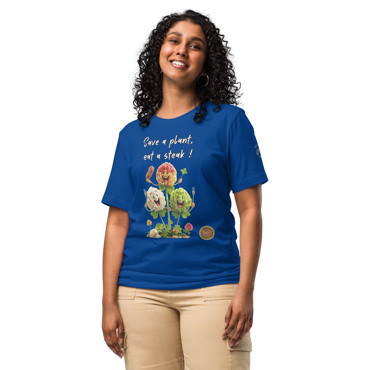 Product mockup. A woman in beige pants wearing a royal blue T-shirt with three smiling cartoon flowers, a steak, and the phrase “Save a plant, eat a steak!”.
