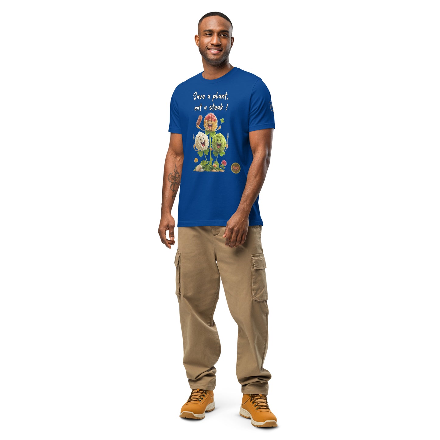 Product mockup. Full-body image of a man posing in tan pants and a royal blue T-shirt decorated with three cartoon flowers, a steak, and “Save a plant, eat a steak!” text.