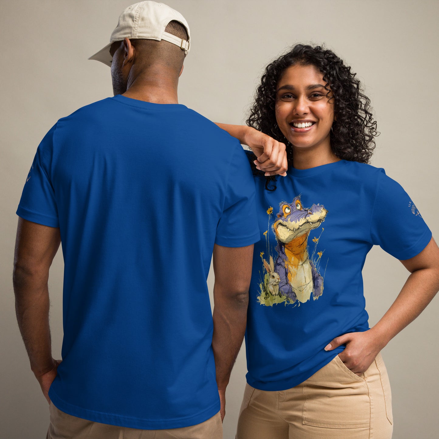 Product mockup. Man and woman in navy t-shirts; man shown from back, woman in beige pants with a blue t-shirt featuring a cartoon purple alligator, yellow flowers, and a bunny, man with back view.