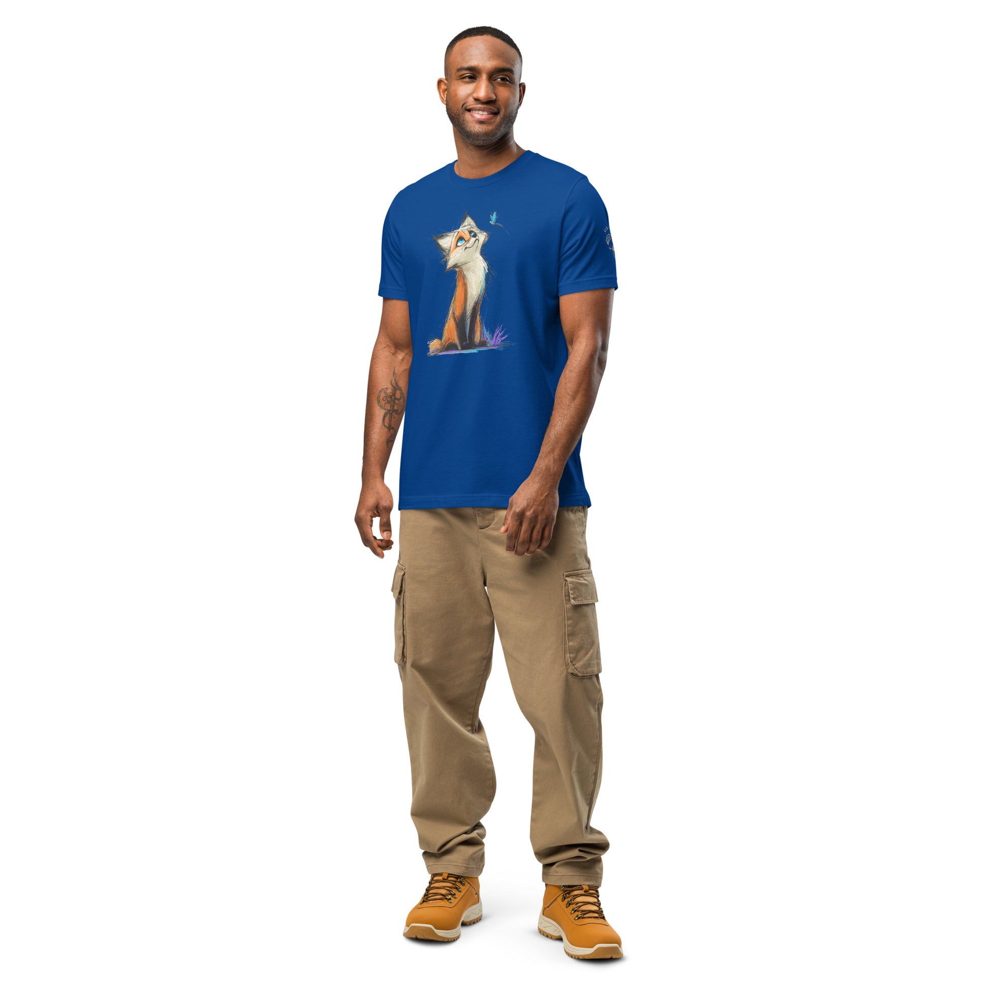 Product mockup. Royal blue T-shirt on a hanger with an orange, white, and brown cartoon fox, seated and looking up at a small blue bird and purple grass.