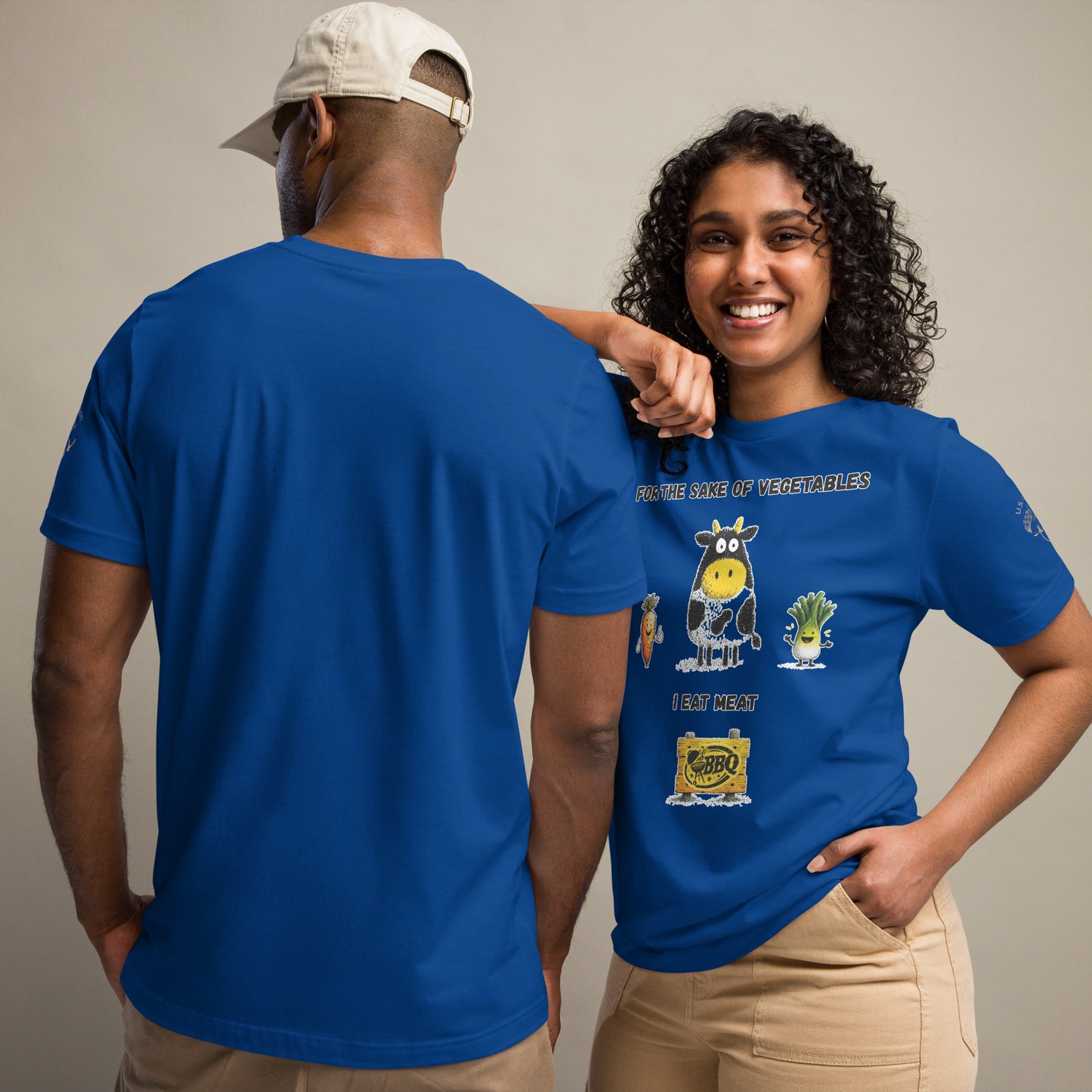 Product mockup. Man and woman in cargo pants, with the woman wearing a blue T-shirt printed with a cartoon cow and veggies, text: “For the sake of vegetables I eat meat.”