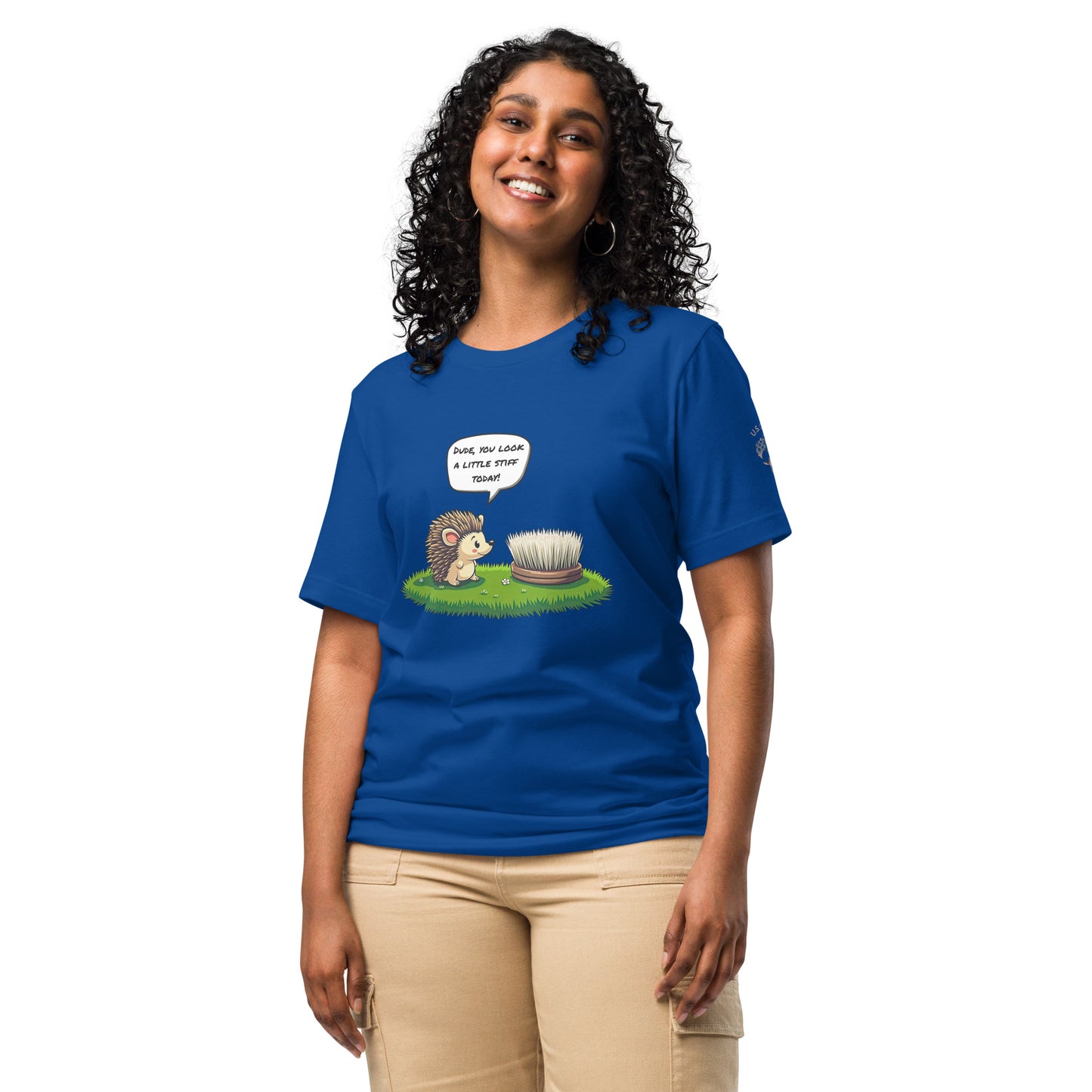Product mockup. Woman in beige pants wearing a blue T-shirt with a hedgehog speaking to a stiff brush in grass, speech bubble says "Dude, you look a little stiff today!"