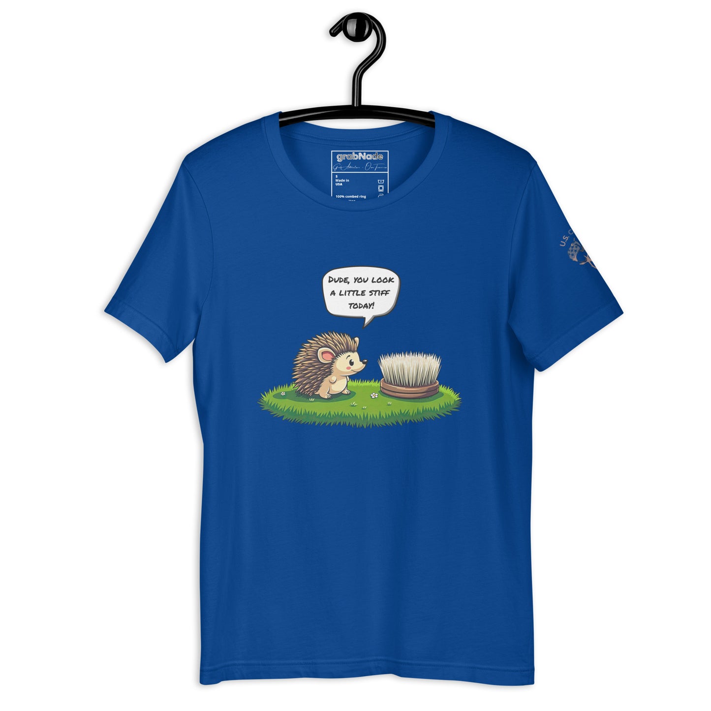 Product mockup. Blue T-shirt on a hanger printed with a cartoon hedgehog talking to a scrubbing brush in grass, saying "Dude, you look a little stiff today!"
