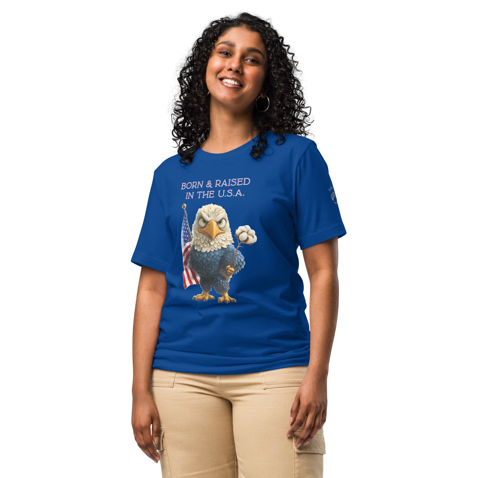 Product mockup. Woman in beige pants wearing a blue T-shirt with a cartoon bald eagle holding a cotton boll and US flag, text reads “Born & Raised in the U.S.A.”