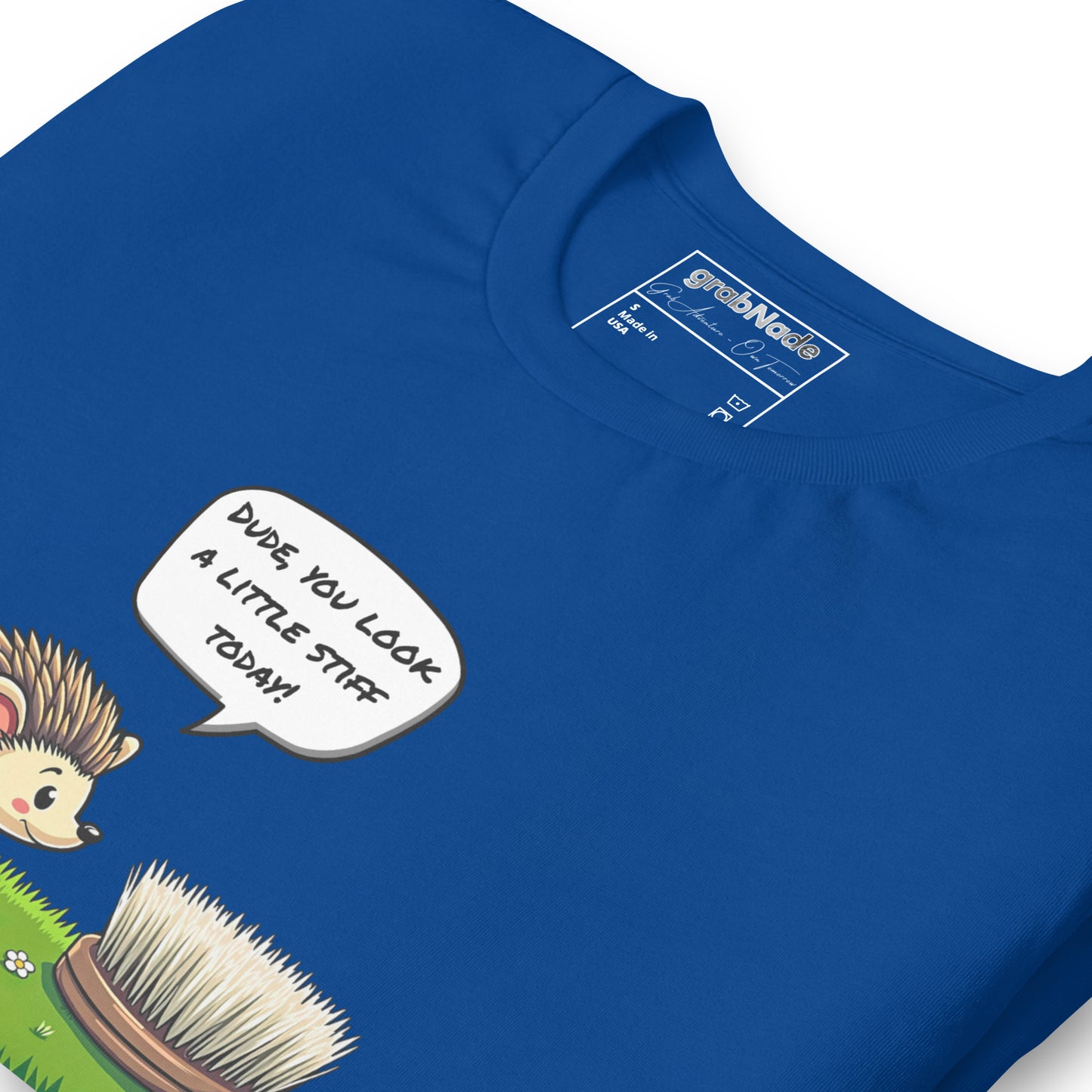 Product mockup. Blue T-shirt, zoomed in, cartoon hedgehog saying “DUDE YOU LOOK A LITTLE STIFF TODAY!” to a brush.