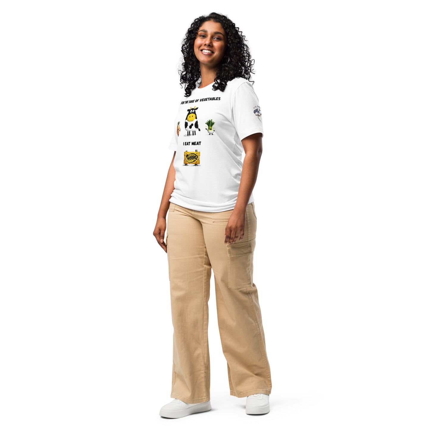 Product mockup. Person standing wearing a white t-shirt displaying cartoon illustrations of a cow, carrot, leek, and cheese, with the text "FOR THE SAKE OF VEGETABLES I EAT MEAT." Beige pants and white shoes.