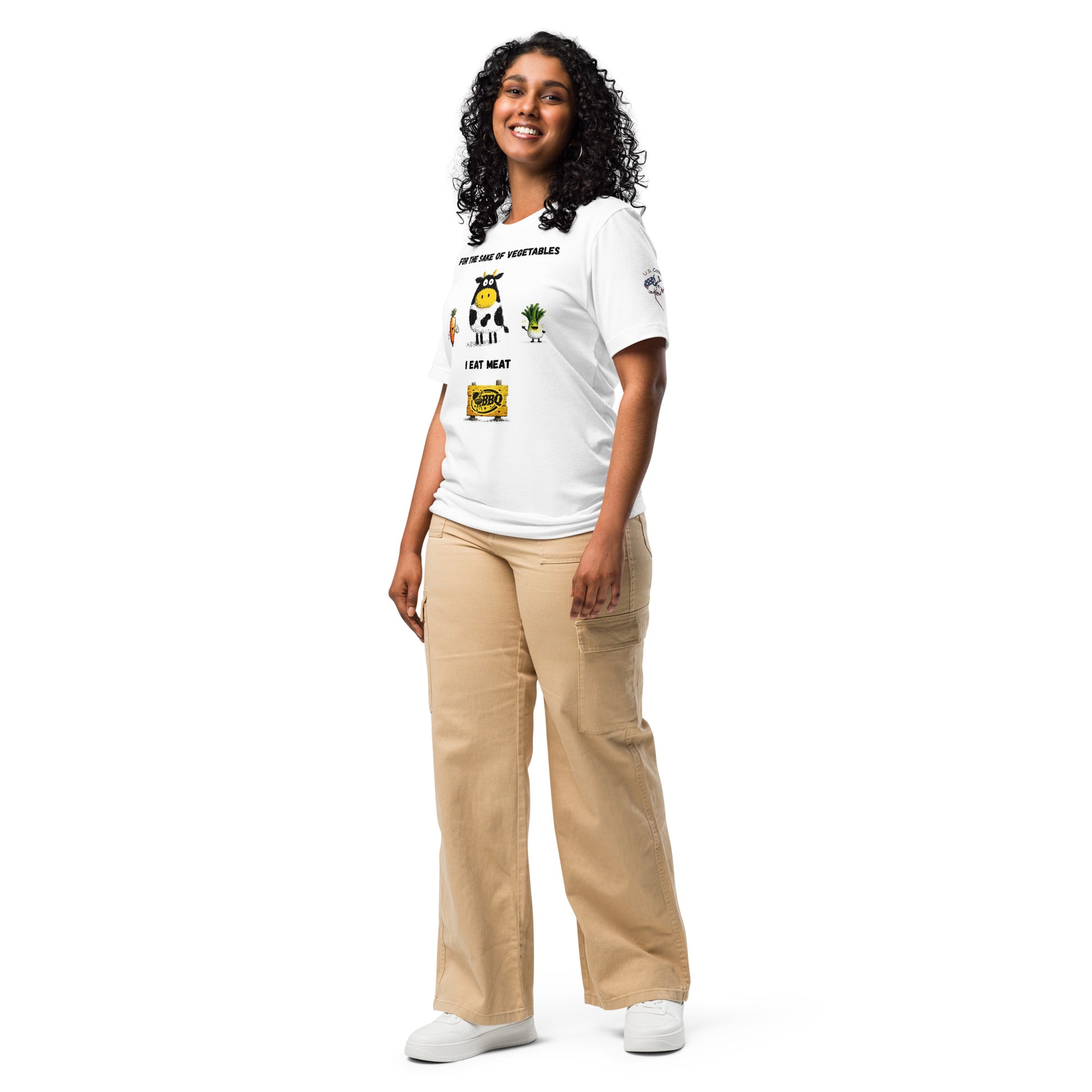 Product mockup. Person standing wearing a white t-shirt displaying cartoon illustrations of a cow, carrot, leek, and cheese, with the text "FOR THE SAKE OF VEGETABLES I EAT MEAT." Beige pants and white shoes.