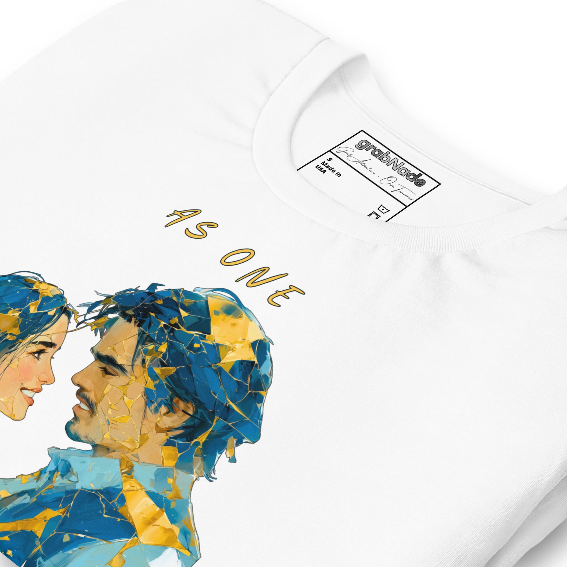 Product mockup. Close-up of a white T-shirt showing two stylized faces of a man and woman made from blue and gold geometric shards, with the text “AS ONE” above.