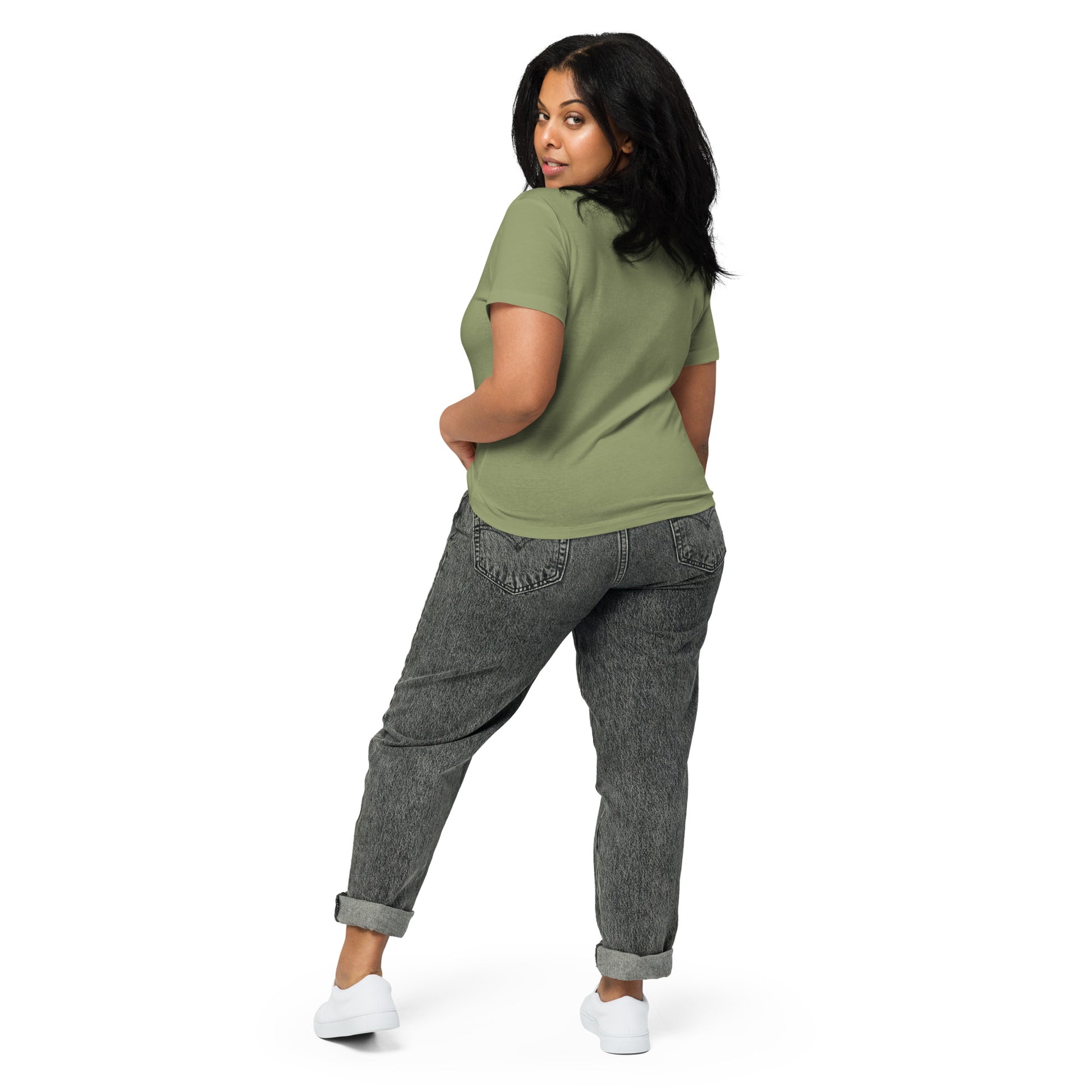 Product mockup. Back view of a woman wearing a light green high-waisted t-shirt and light-colored pants. The back of the shirt is plain with no graphics or text, and she is turning her head to look at the camera, set against a clean white backdrop.