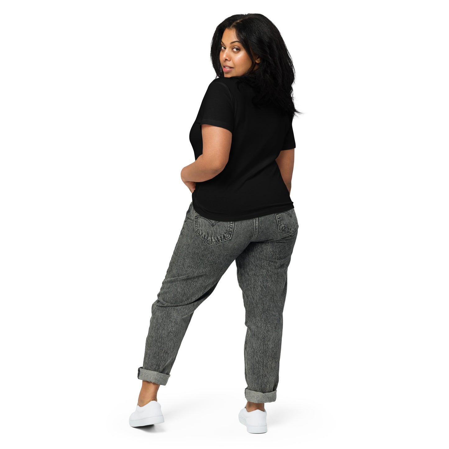 Product mockup. Back view of a woman wearing a black high-waisted t-shirt and light-colored pants. The back of the shirt is plain with no graphics or text, and she is turning her head to look at the camera, set against a clean white backdrop.
