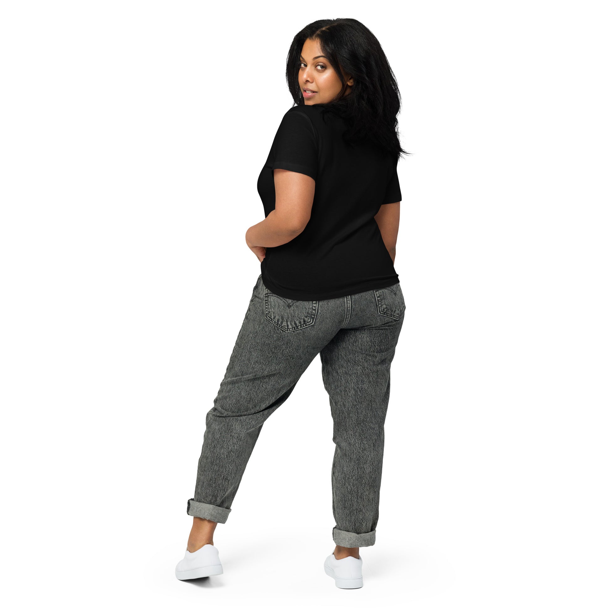 Product mockup. Back view of a woman wearing a black high-waisted t-shirt and light-colored pants. The back of the shirt is plain with no graphics or text, and she is turning her head to look at the camera, set against a clean white backdrop.