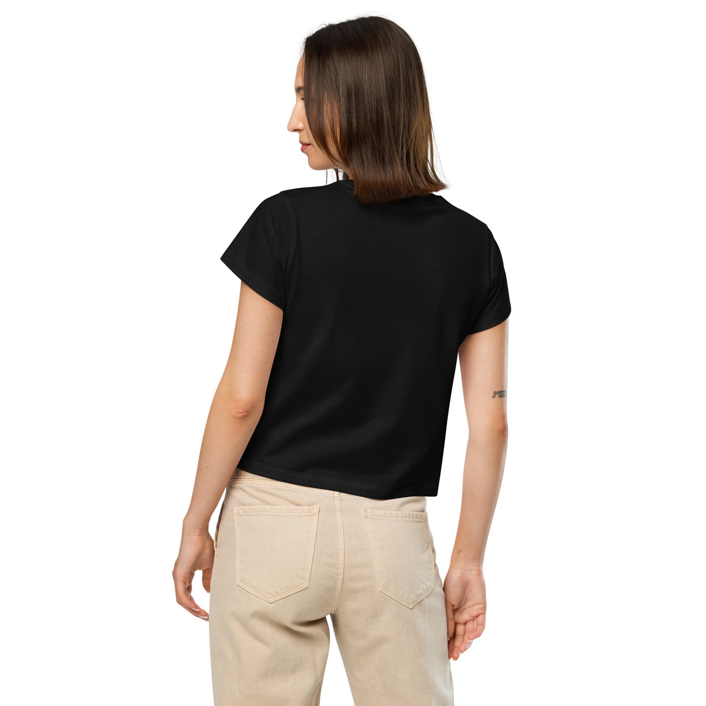 Product mockup. Back view of a woman wearing a black high-waisted t-shirt and beige pants. The back of the t-shirt is plain, and she is facing away from the camera, standing against a simple white background.