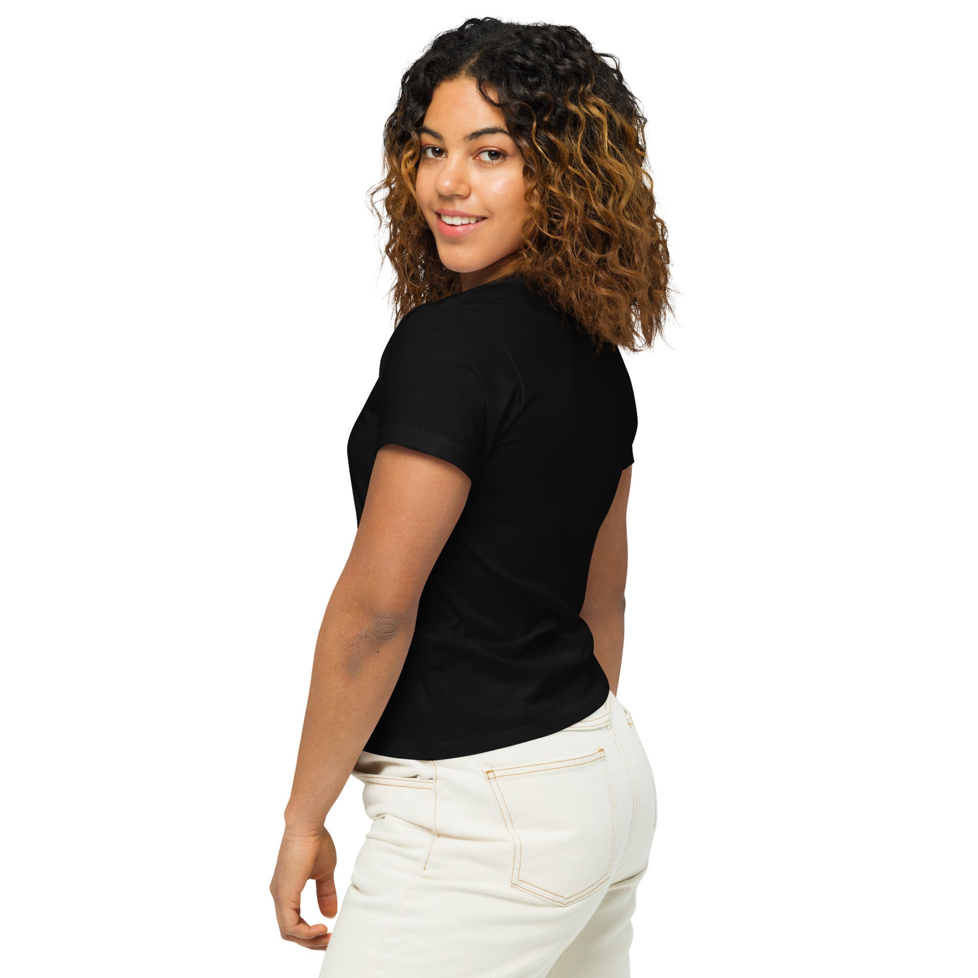Product mockup. Back view of a woman wearing a black high-waisted t-shirt and light-colored pants. The back of the shirt is plain with no graphics or text, and she is turning her head to look at the camera, set against a clean white backdrop.
