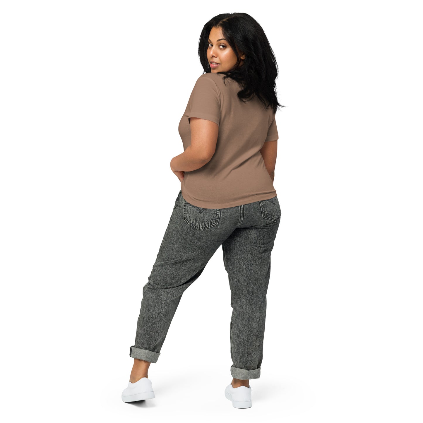 Product mockup. Back view of a woman wearing a latte high-waisted t-shirt and light-colored pants. The back of the shirt is plain with no graphics or text, and she is turning her head to look at the camera, set against a clean white backdrop.