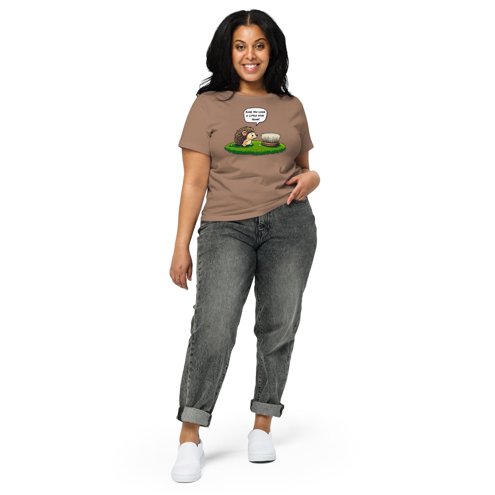 Product mockup. Full-body view of a woman standing and wearing a brown high-waisted t-shirt with the hedgehog and scrubbing brush cartoon graphic on the front. She is also wearing relaxed-fit gray jeans and white shoes. The setting is a plain white background.