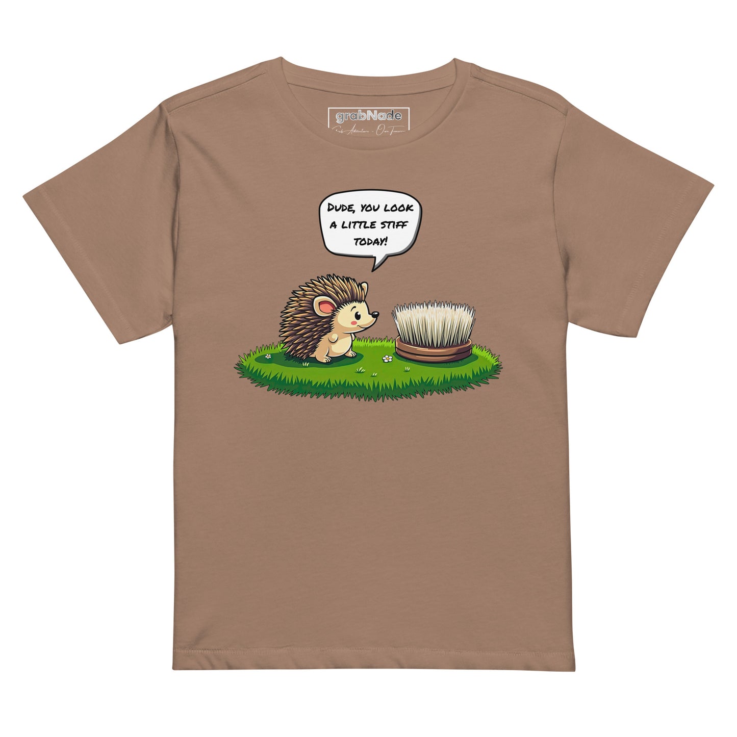 Product mockup. Latte high-waisted women's t-shirt laid flat against a plain background. A colorful cartoon graphic of a hedgehog with a speech bubble—'Dude, you look a little stiff today!'—faces a scrubbing brush on grass. The shirt label at the collar reads 'grabNade.