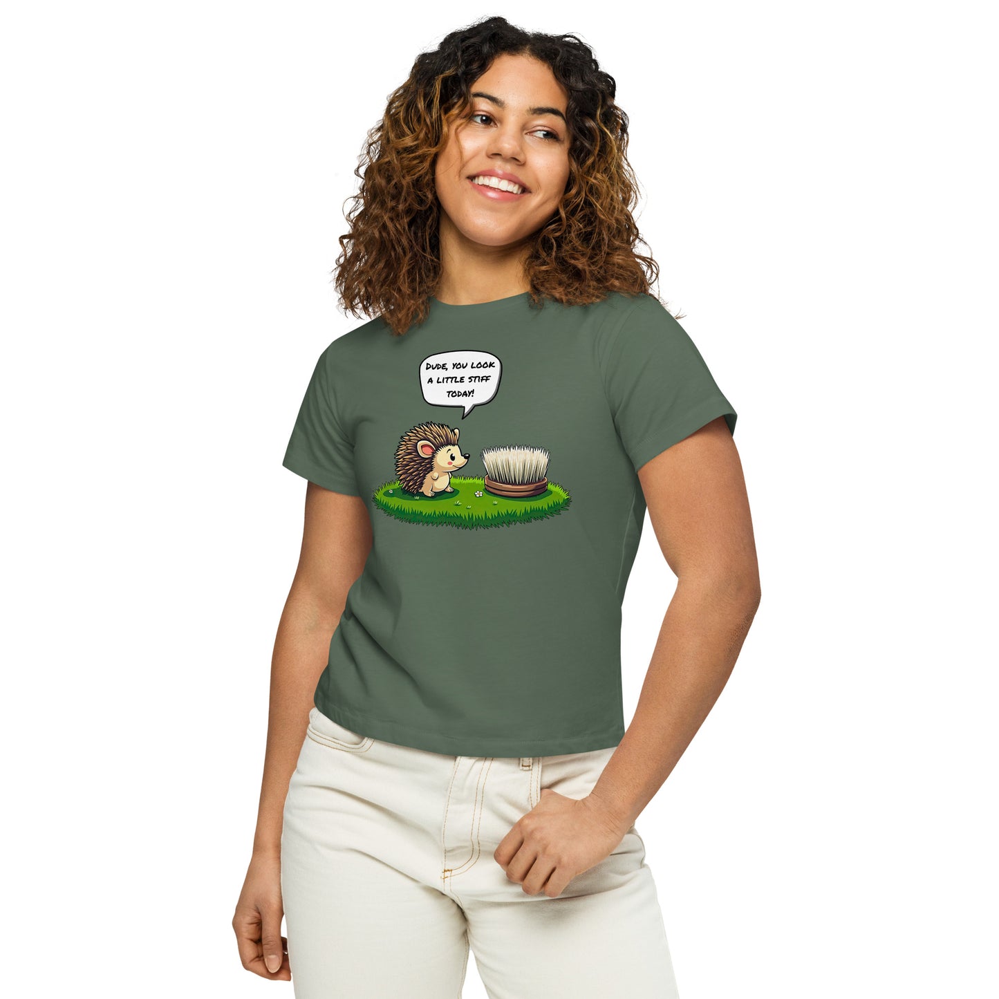 Product mockup. Close-up, front view of a woman in a green pine high-waisted t-shirt with a playful hedgehog and scrubbing brush design. She has curly hair, is smiling, and wears light-colored jeans, posing against a white background.