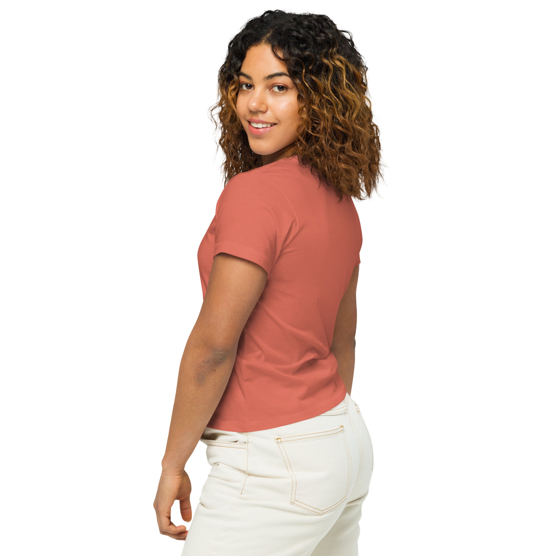 Product mockup. Back view of a woman wearing a red sorbet high-waisted t-shirt and light-colored pants. The back of the shirt is plain with no graphics or text, and she is turning her head to look at the camera, set against a clean white backdrop.