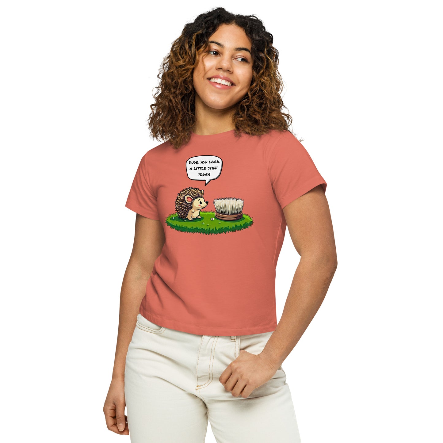 Product mockup. Close-up, front view of a woman in a red sorbet high-waisted t-shirt with a playful hedgehog and scrubbing brush design. She has curly hair, is smiling, and wears light-colored jeans, posing against a white background.