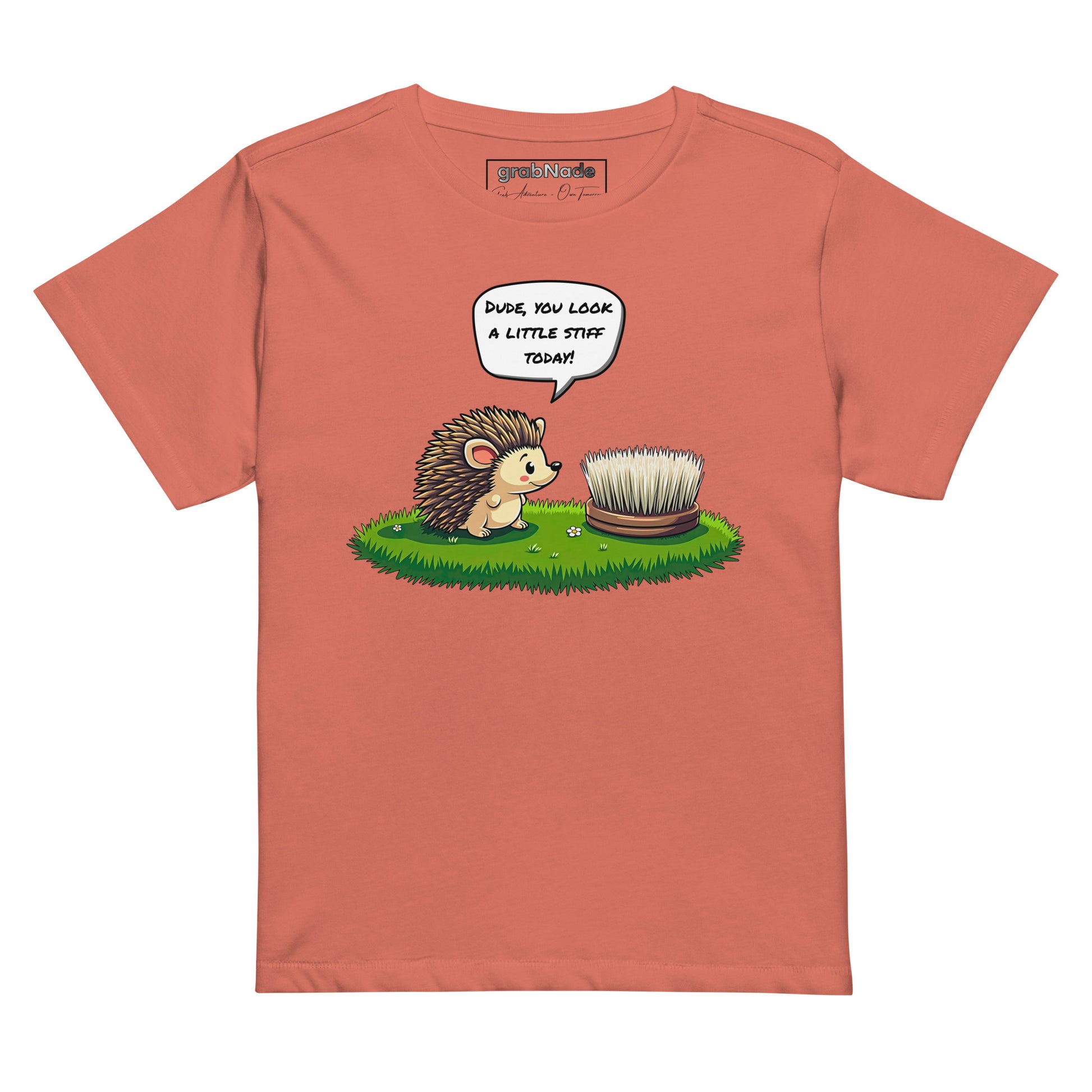 Product mockup. Red sorbet high-waisted women's t-shirt laid flat against a plain background. A colorful cartoon graphic of a hedgehog with a speech bubble—'Dude, you look a little stiff today!'—faces a scrubbing brush on grass. The shirt label at the collar reads 'grabNade.