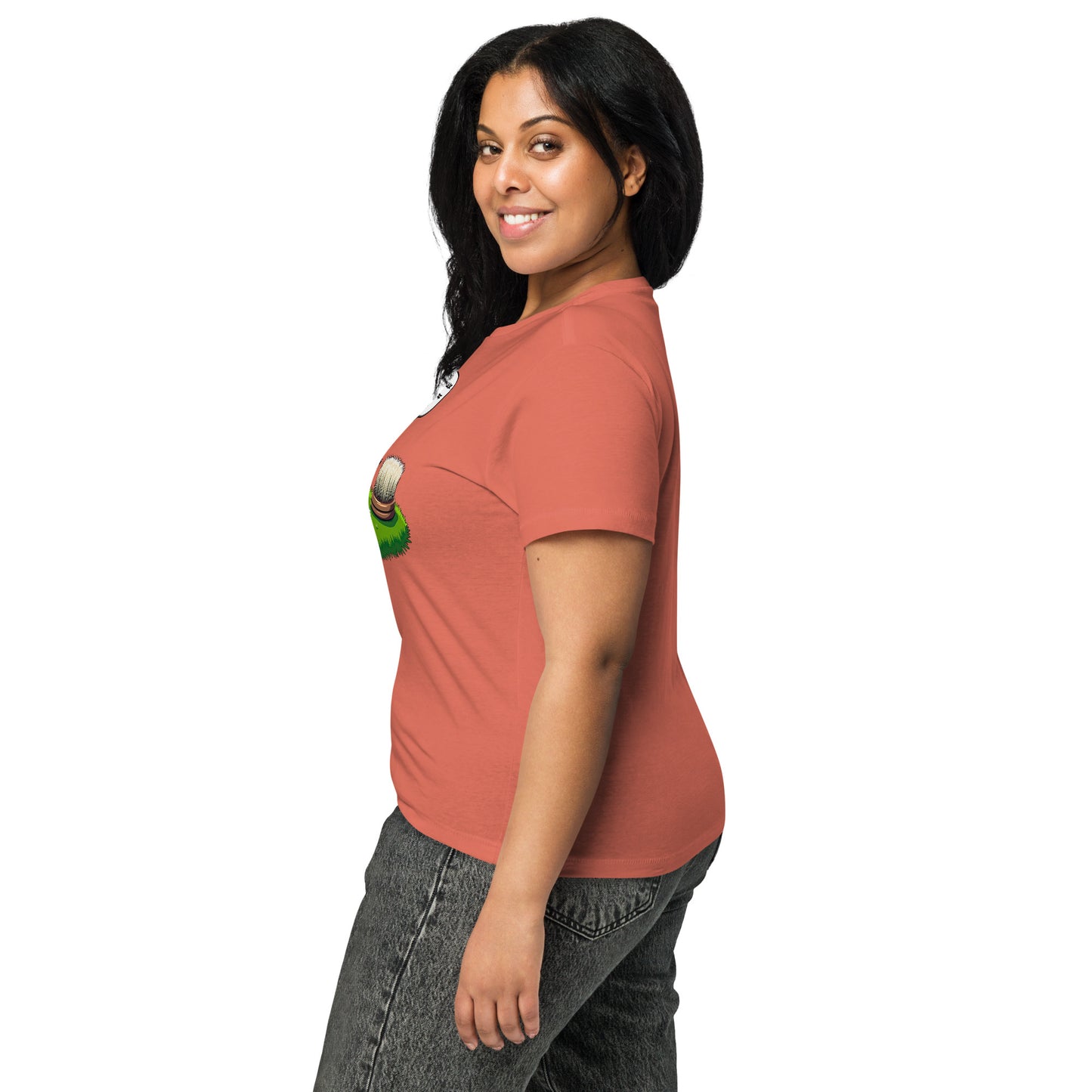 Product mockup. Side view of a woman wearing a red sorbet high-waisted t-shirt with a colorful cartoon graphic featuring a hedgehog and a scrubbing brush, and fitted gray jeans. She is smiling and standing against a simple white background.