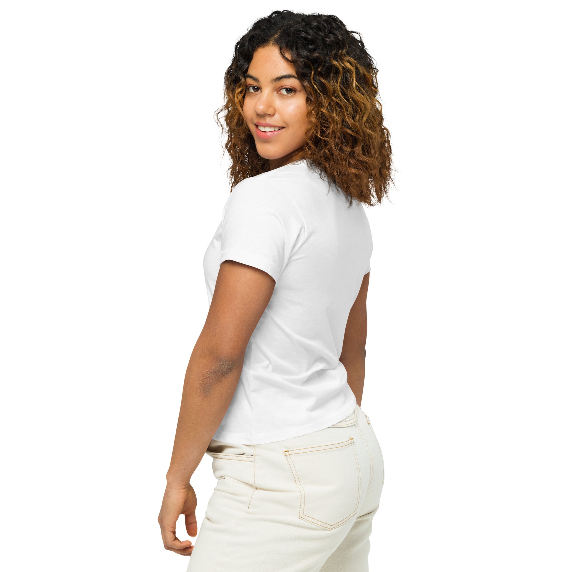 Product mockup. Back view of a woman wearing a white high-waisted t-shirt and light-colored pants. The back of the shirt is plain with no graphics or text, and she is turning her head to look at the camera, set against a clean white backdrop.