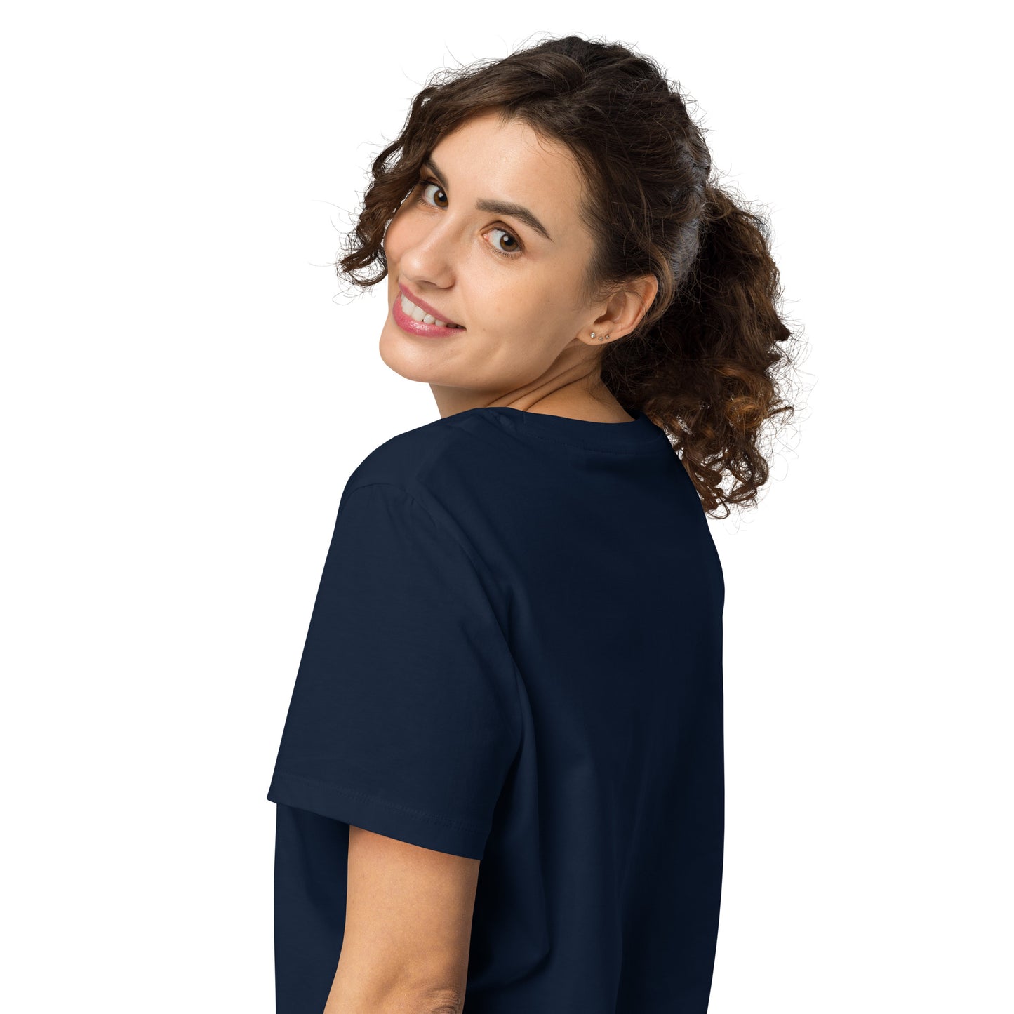 Product mockup. A woman with curly brown hair in a ponytail, shown from behind and looking over her shoulder with a smile, wearing a plain navy blue organic cotton t-shirt. The shirt has a soft, regular fit and no visible design on the back.