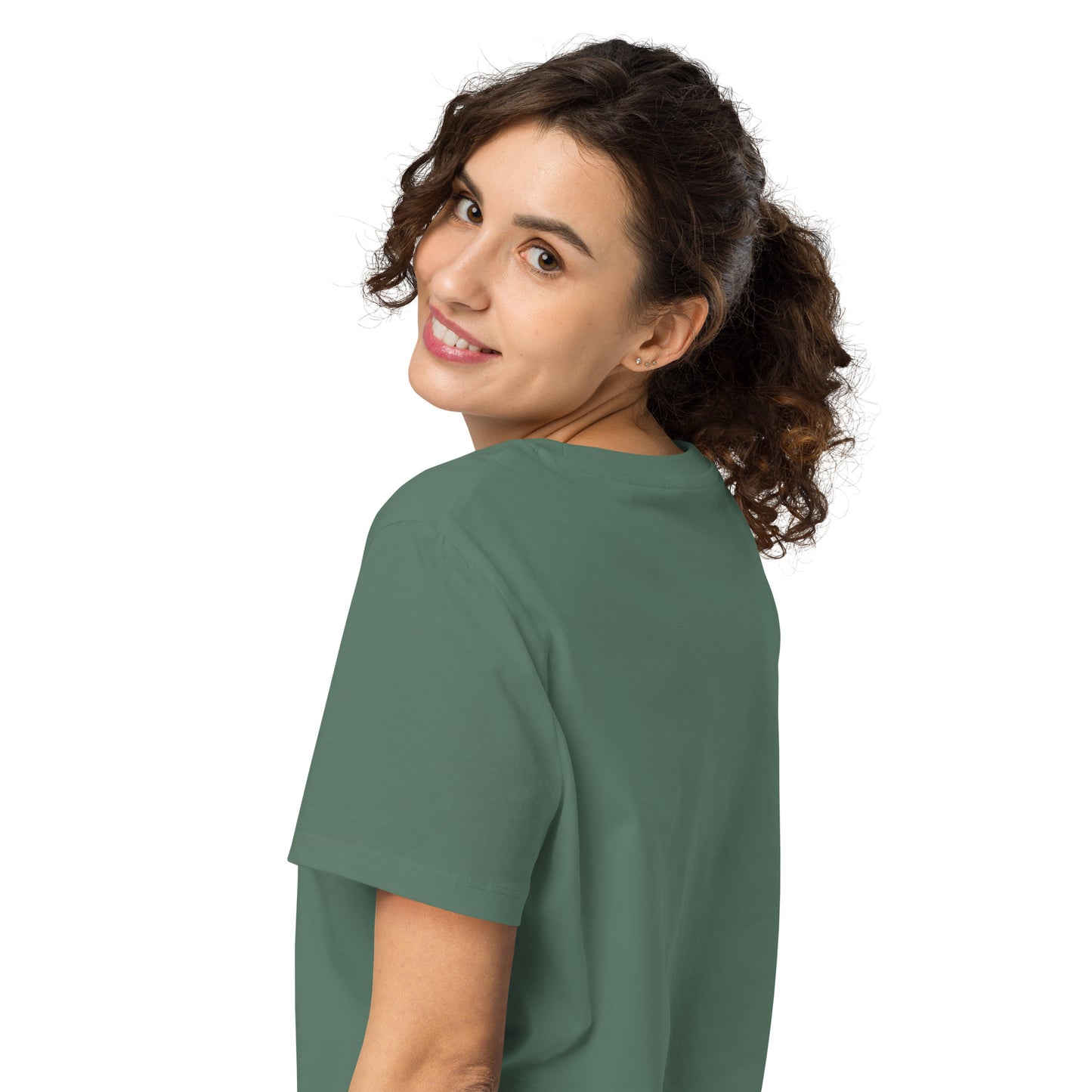 Product mockup. A woman with curly brown hair in a ponytail, shown from behind and looking over her shoulder with a smile, wearing a plain green organic cotton t-shirt. The shirt has a soft, regular fit and no visible design on the back.