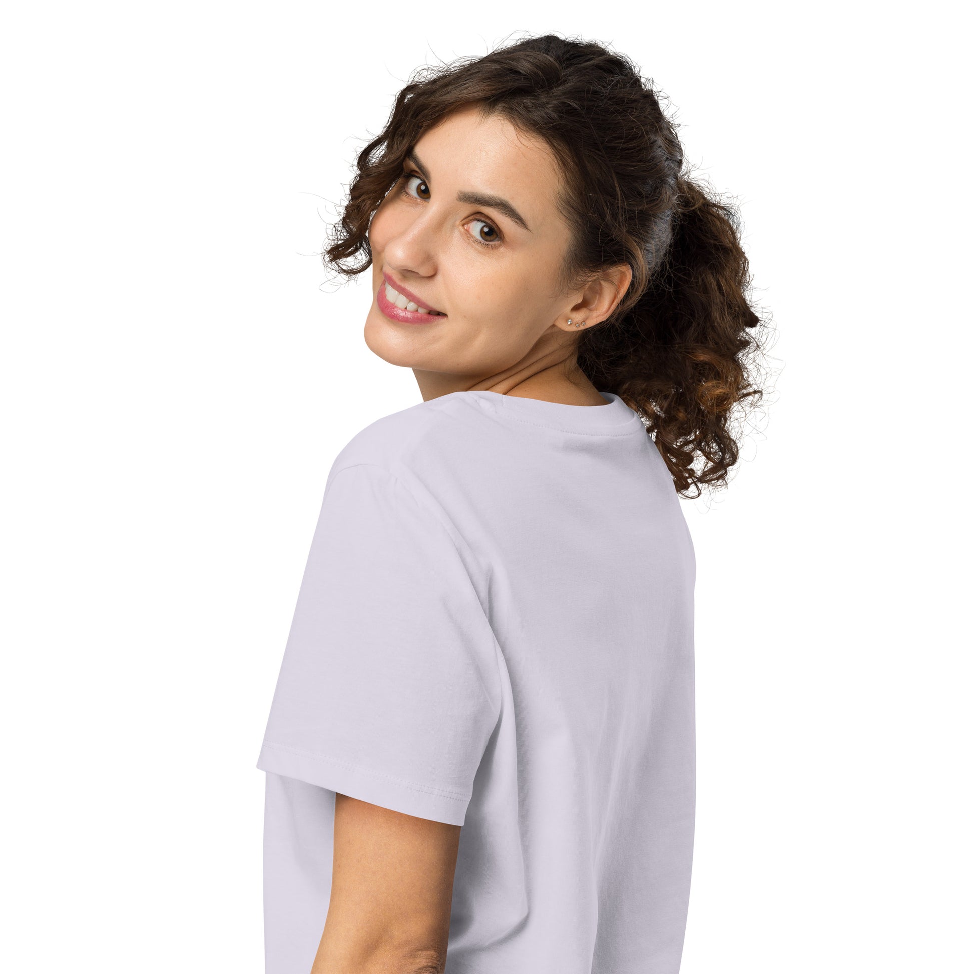 Product mockup. A woman with curly brown hair in a ponytail, shown from behind and looking over her shoulder with a smile, wearing a plain lavender organic cotton t-shirt. The shirt has a soft, regular fit and no visible design on the back.