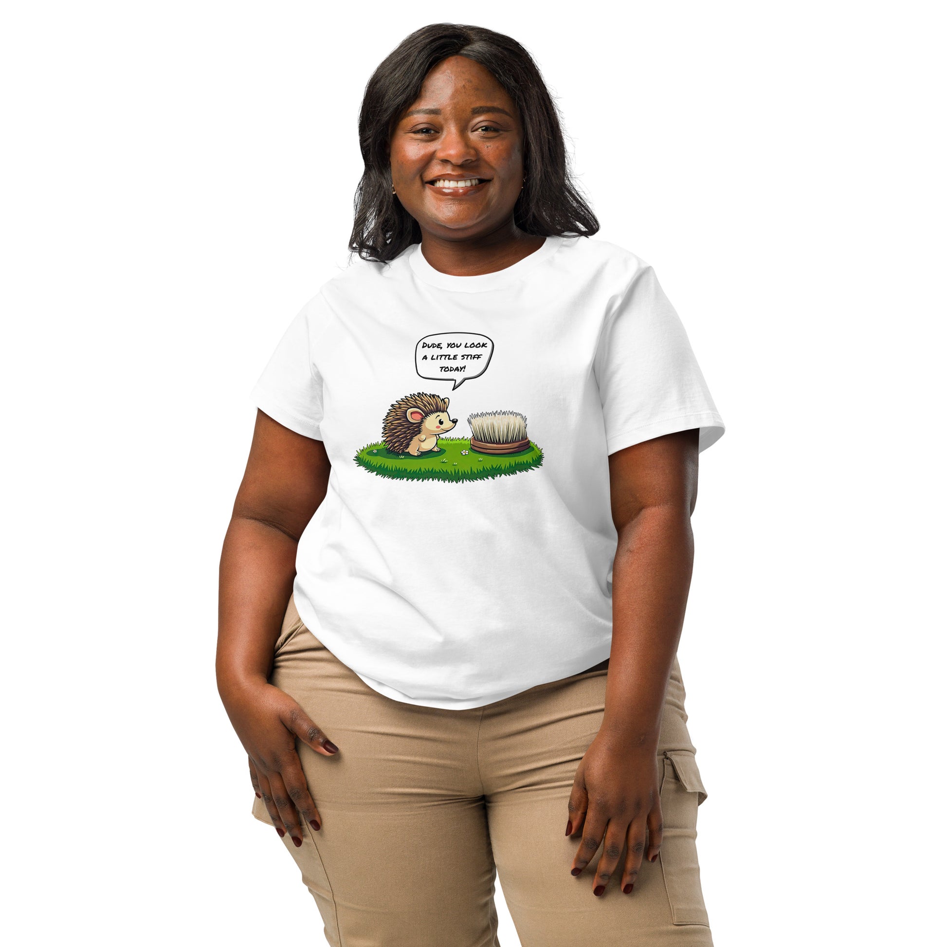 Product mockup. A happy woman wearing a 2XL white organic cotton t-shirt featuring a playful cartoon illustration of a hedgehog standing on green grass beside a scrubbing brush. The hedgehog has a speech bubble that says, 'DUDE, YOU LOOK A LITTLE STIFF TODAY!'