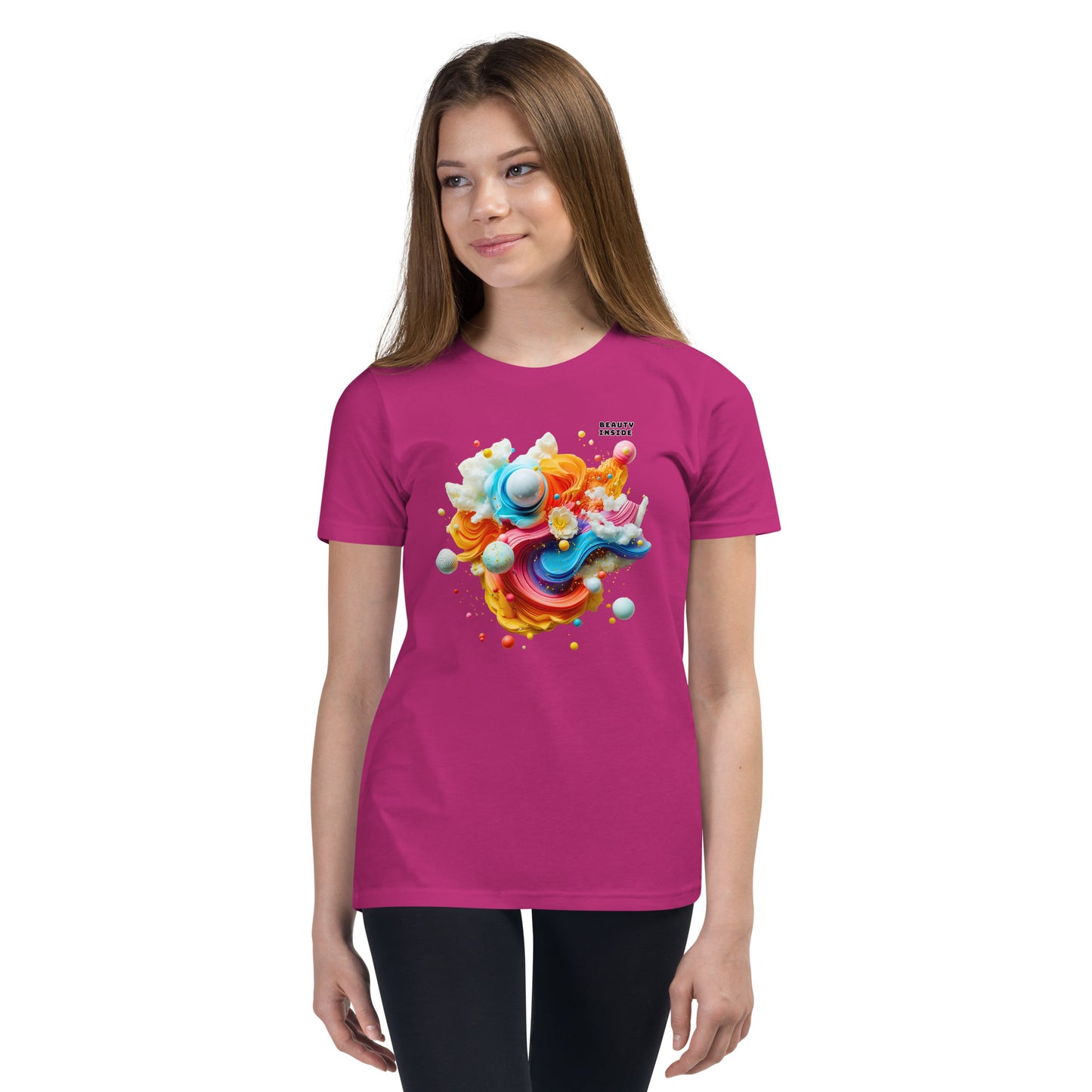 Product mockup. A young girl wearing a pink youth ultra-soft premium t-shirt with a colorful, abstract modern art design on the front. The design includes vibrant swirls and spheres in blue, pink, orange, yellow, and white, with a small 'BEAUTY INSIDE' text near the upper right part of the graphic. She is paired with black leggings and looking slightly to the side with a subtle smile.