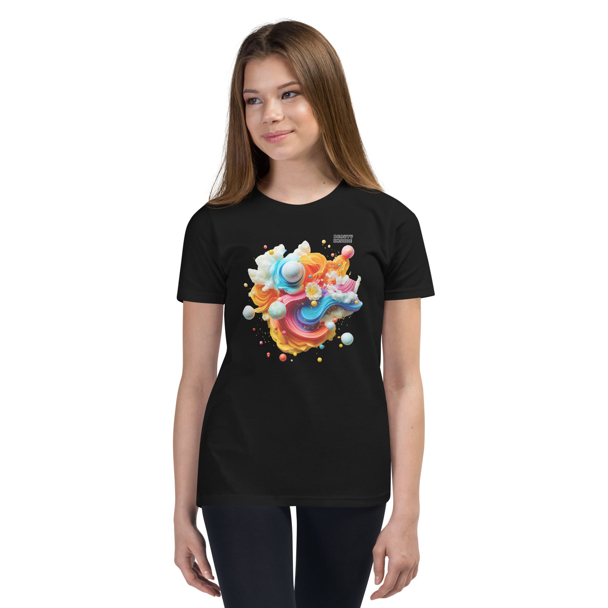 Product mockup. A young girl wearing a black youth ultra-soft premium t-shirt with a colorful, abstract modern art design on the front. The design includes vibrant swirls and spheres in blue, pink, orange, yellow, and white, with a small 'BEAUTY INSIDE' text near the upper right part of the graphic. She is paired with black leggings and looking slightly to the side with a subtle smile.