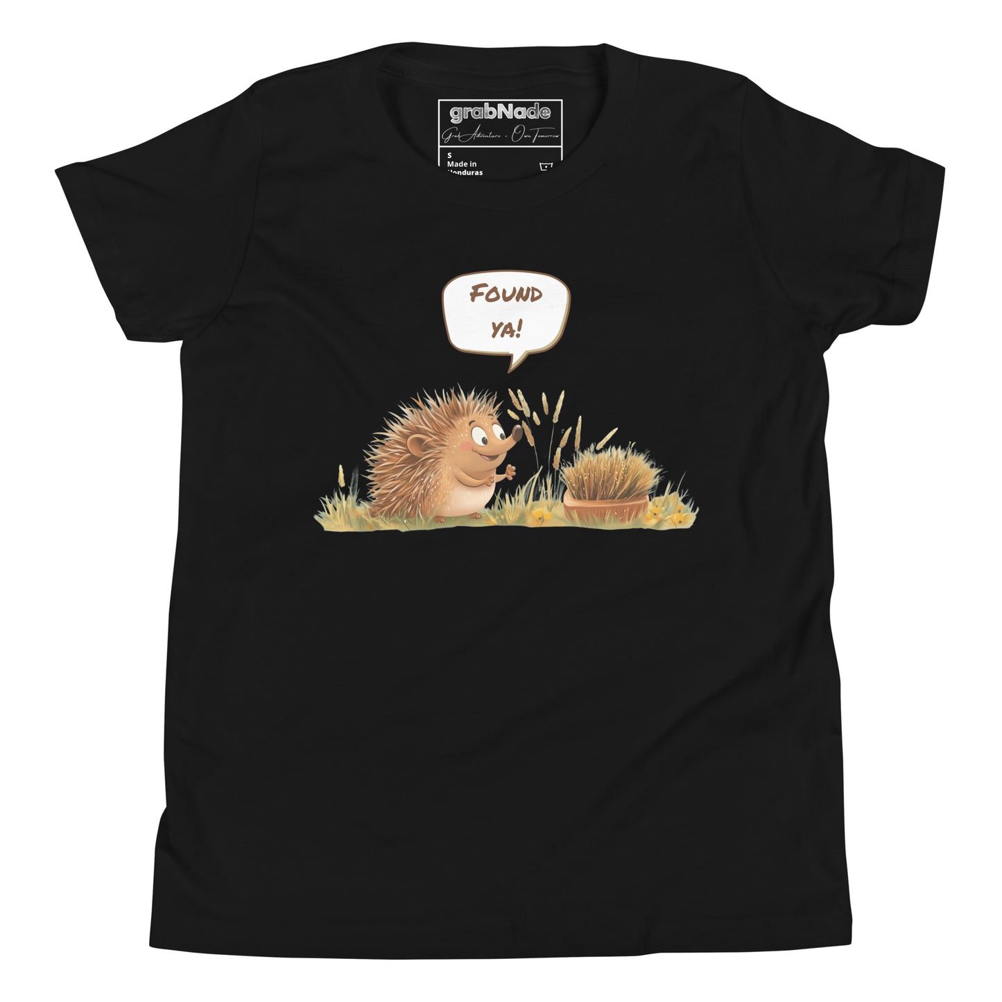 Product mockup. A smiling child wearing a black t-shirt printed with a playful illustration of a cheerful hedgehog popping up from the grass and saying “Found ya!” in a speech bubble, beside a second hedgehog curled into a ball, all set against a clean studio background.