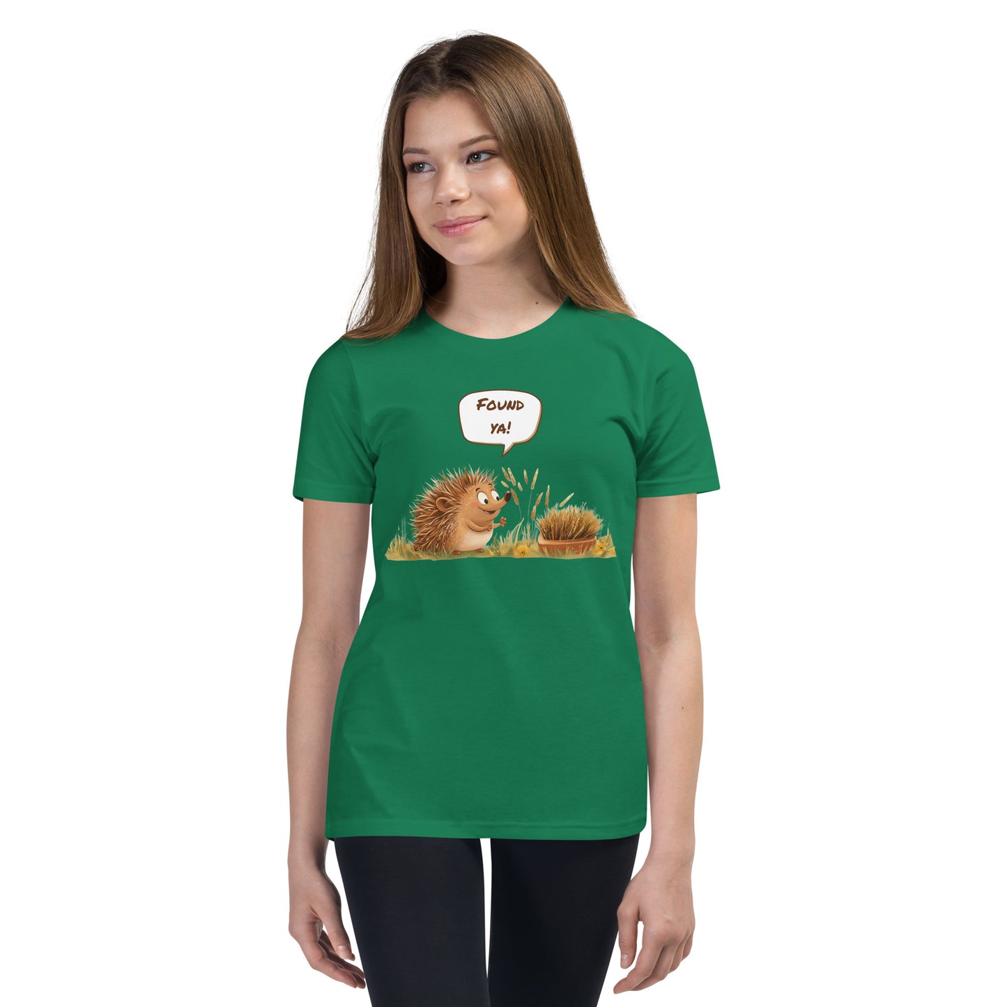 Product mockup. Ultra-soft premium youth green t-shirt featuring cute cartoon hedgehog with speech bubble saying 'FOUND YA!' over grassy ground, in front of a brush, modeled on young girl.