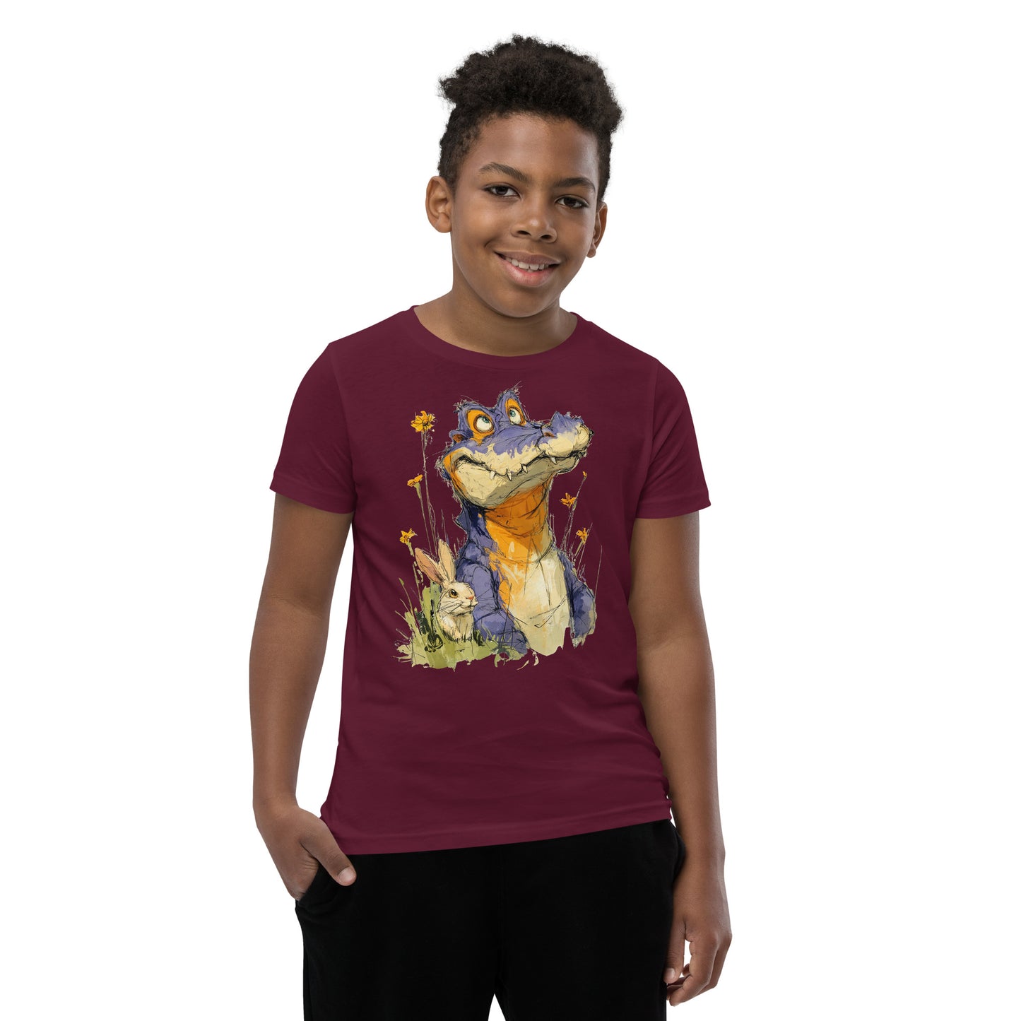 Product mockup.  A smiling child wearing a maroon t‑shirt featuring a whimsical sketch of a purple alligator with orange accents sitting in tall grass beside a white rabbit and yellow wildflowers, set against a clean studio background.