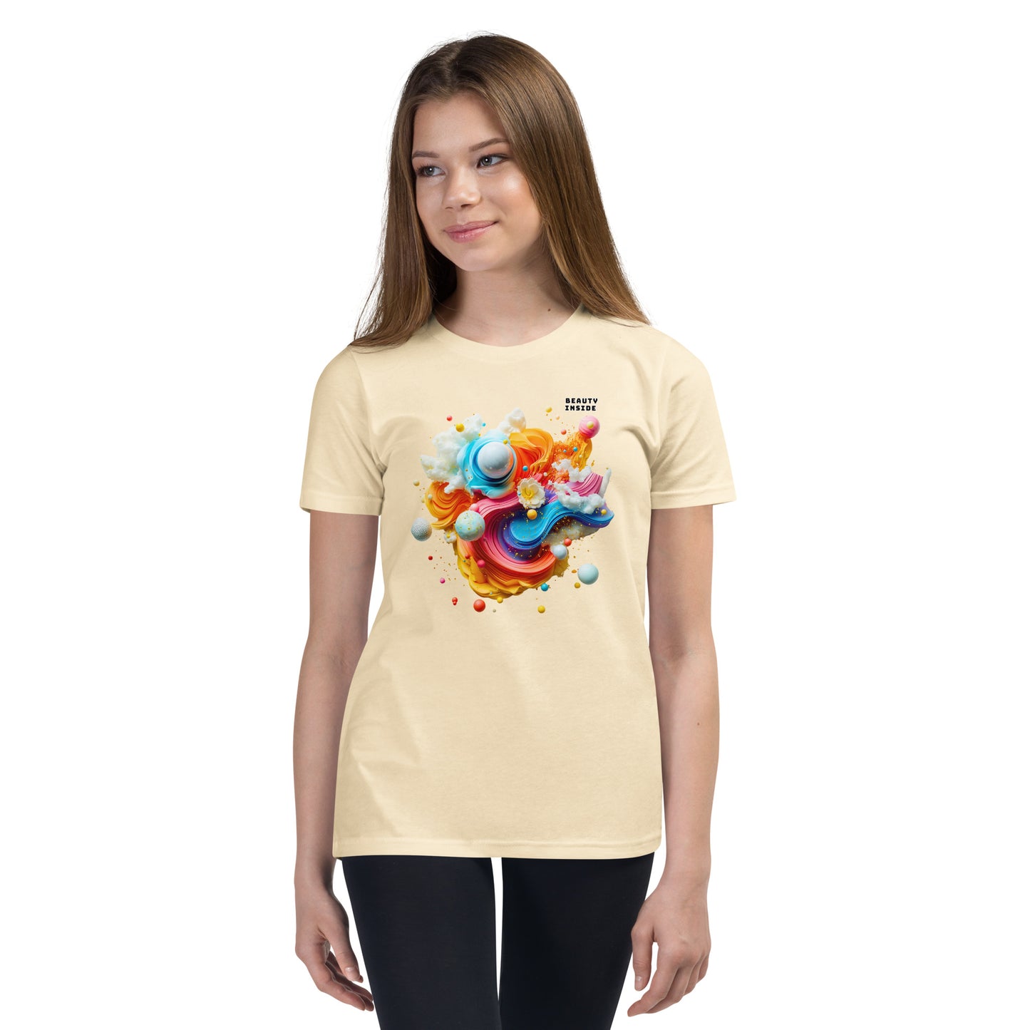 Product mockup. A young girl wearing a beige youth ultra-soft premium t-shirt with a colorful, abstract modern art design on the front. The design includes vibrant swirls and spheres in blue, pink, orange, yellow, and white, with a small 'BEAUTY INSIDE' text near the upper right part of the graphic. She is paired with black leggings and looking slightly to the side with a subtle smile.