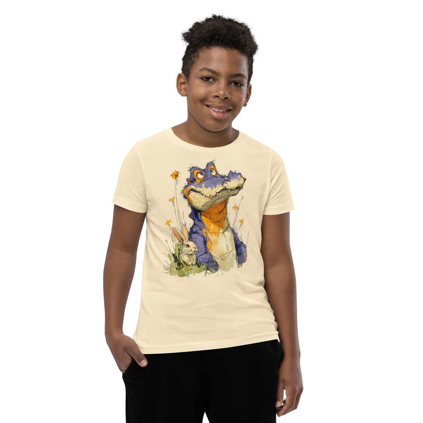 Product mockup.  A smiling child wearing a beige t‑shirt featuring a whimsical sketch of a purple alligator with orange accents sitting in tall grass beside a white rabbit and yellow wildflowers, set against a clean studio background.