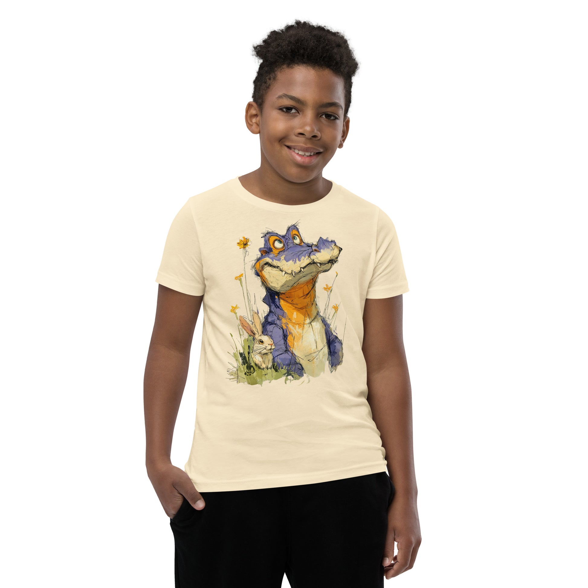 Product mockup.  A smiling child wearing a beige t‑shirt featuring a whimsical sketch of a purple alligator with orange accents sitting in tall grass beside a white rabbit and yellow wildflowers, set against a clean studio background.