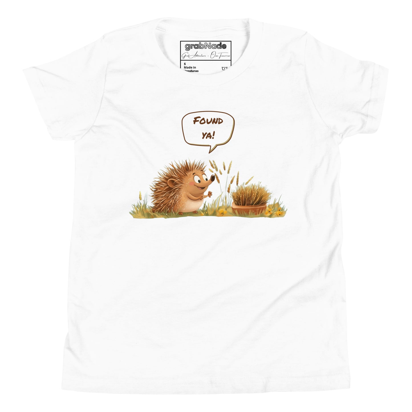 Product mockup. Ultra-soft premium youth white t-shirt featuring cute cartoon hedgehog with speech bubble saying 'FOUND YA!' over grassy ground, in front of a brush.